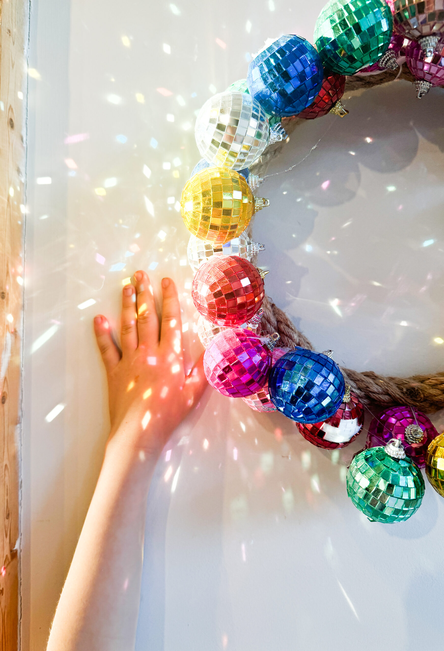 Child's hand touching a vibrant disco ball wreath, a fun DIY craft for kids and parents.